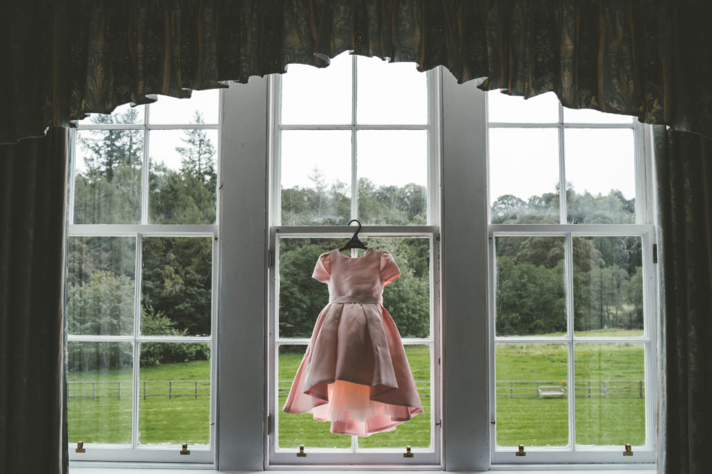 a blush pink flower girl dress is framed in a curtained window