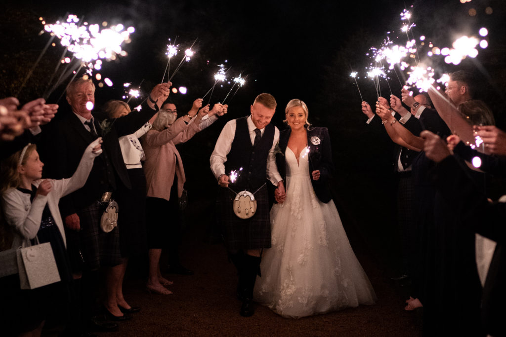 newly wed couple walk through a sparkler exit held by friends and family
